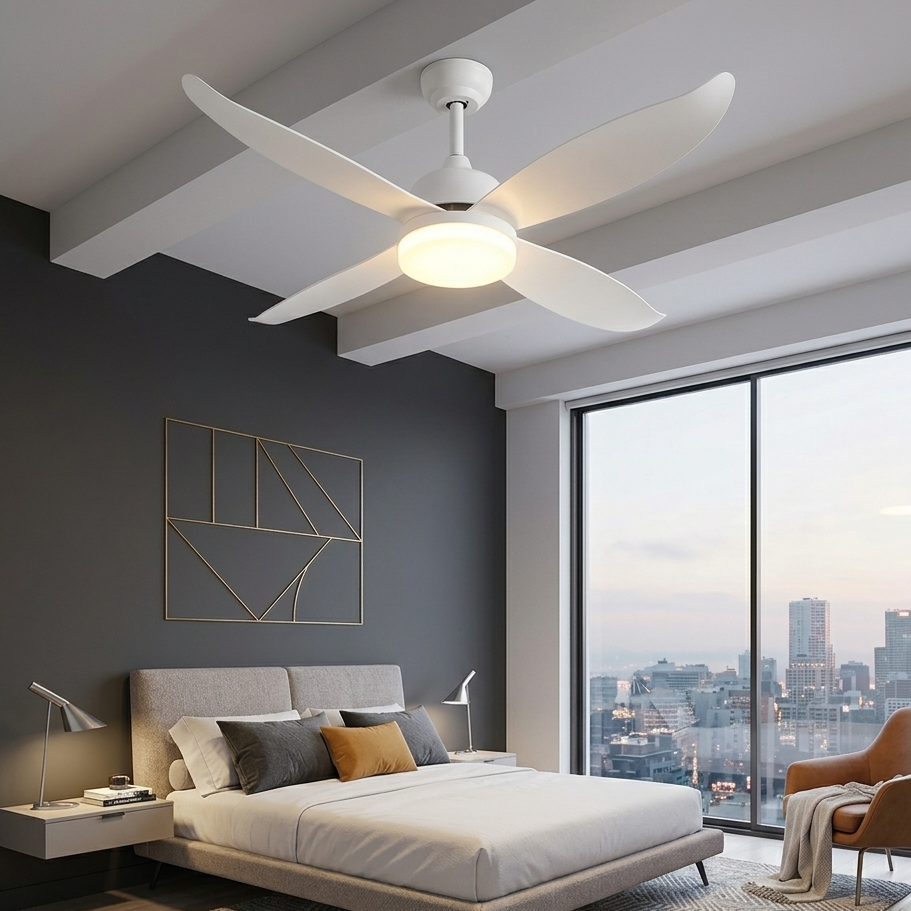 A modern bedroom interior featuring a white ceiling fan with integrated light fixture mounted on a white ceiling. The room includes a low bed with white bedding, gray accent pillows, a textured beige rug, a dark gray accent wall with gold geometric wall art, and a large floor-to-ceiling window overlooking a city skyline.